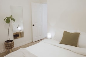 Una camera da letto con un letto, un comodino, una lampada, uno specchio e una pianta in vaso.
