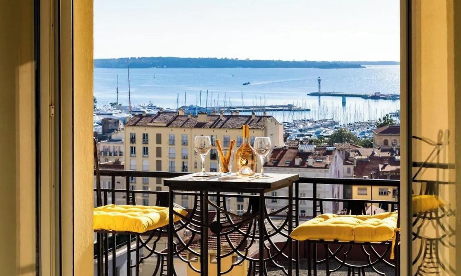 Een balkon met een tafel voor twee, met uitzicht op een jachthaven vol boten en gebouwen.
