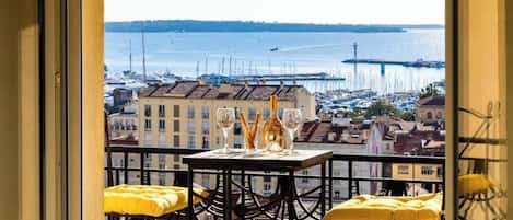 A balcony with a table set for two, overlooking a marina with boats and buildings.