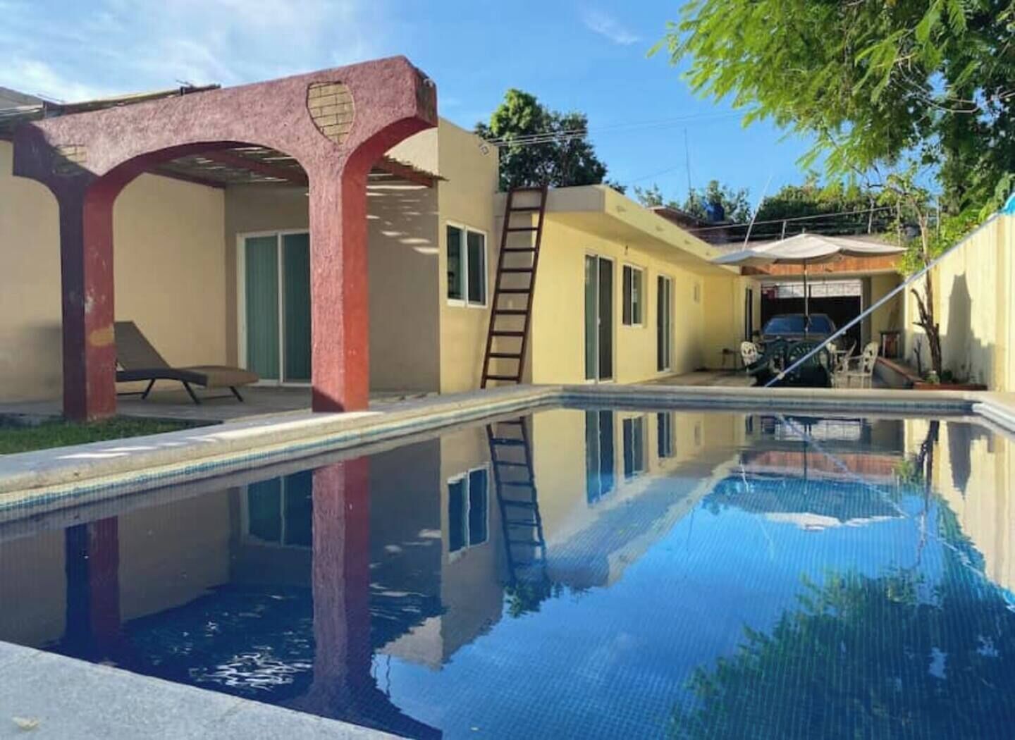 Una piscina con un reflejo claro, una estructura en arco rojo y un vehículo estacionado al fondo.
