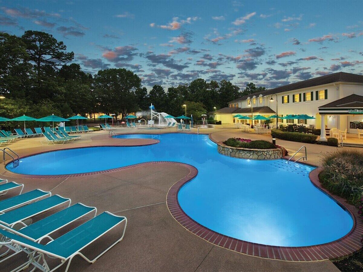 A swimming pool with lounge chairs, a water slide, and a building with a sign.