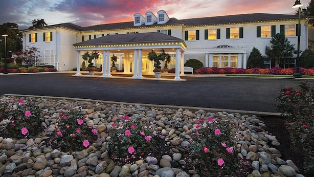 Un hotel con ingresso coperto, un giardino fiorito di fiori rosa e un cielo al tramonto.