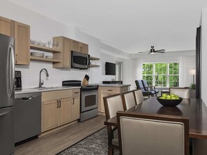 Een moderne keuken met houten kastjes, roestvrijstalen apparatuur en een eethoek met een tafel en stoelen.