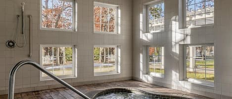 A spa room with a hot tub, large windows, and a wooden floor.