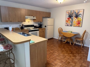 A compact kitchen with wooden cabinets, a stove, sink, and a dining area with a table and chairs. - Central to Spanish Springs & Lake Sumter, golf cart (Lady Lake)