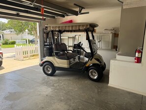 A golf cart parked in a garage with a white fence outside. - Central to Spanish Springs & Lake Sumter, golf cart (Lady Lake)