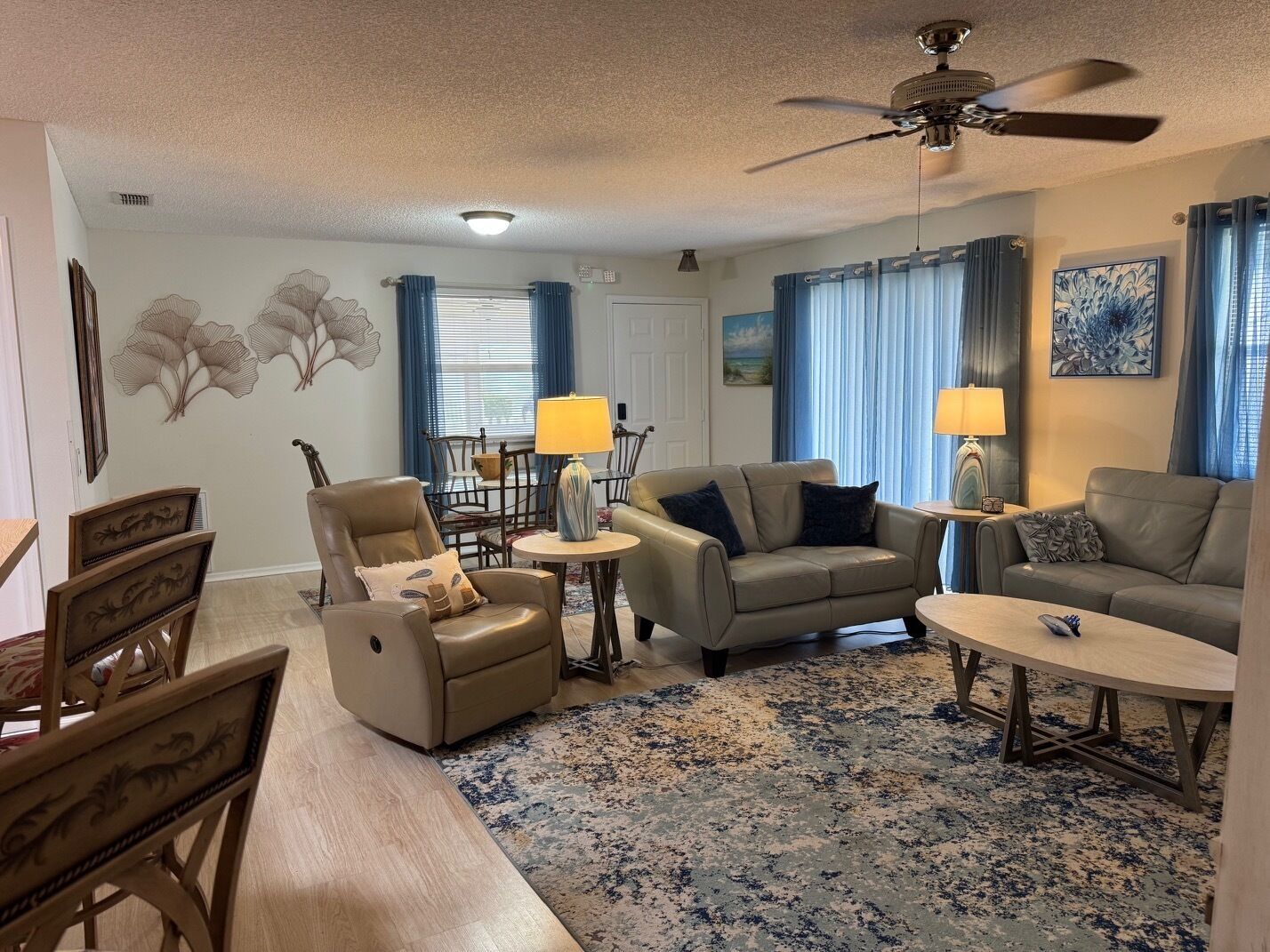 Un salon avec un ventilateur de plafond, un canapé, un fauteuil, une petite table et un tapis.