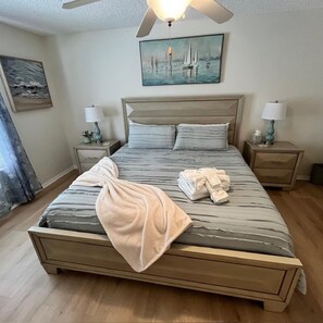 A neatly made bed with a striped bedspread, two bedside tables with lamps, a ceiling fan, and a painting of sailboats on the wall. - Minutes from Spanish Springs & Lake Sumter Landing - Golf Cart Included (Lady Lake)
