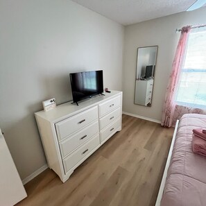 A bedroom with a bed, a dresser with a television, a mirror, and a window with curtains. - Central to Spanish Springs & Lake Sumter, golf cart (Lady Lake)
