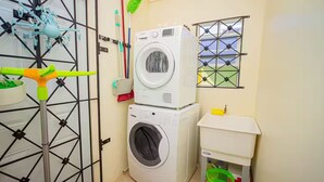 A laundry room with two stacked washing machines, a drying rack, a broom, and a window with a view. - Modern 3BRVilla in Secure Draxhall Gated Community (St Ann)