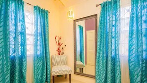 A bathroom with teal curtains, a chair, a mirror, and a vase with branches. - Modern 3BRVilla in Secure Draxhall Gated Community (St Ann)