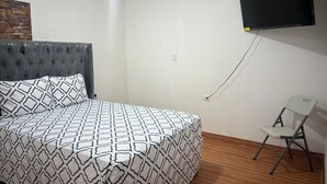 Een slaapkamer met een bed, een aan de muur bevestigde televisie, een stoel en een houten vloer.