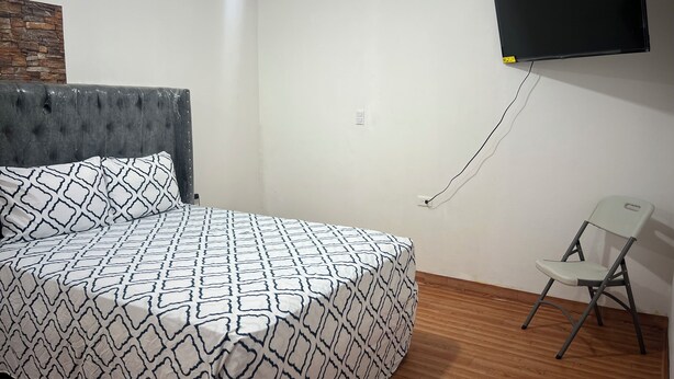 Een slaapkamer met een bed, een aan de muur bevestigde televisie, een stoel en een houten vloer.
