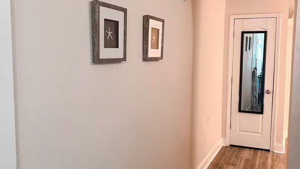 A hallway with wooden flooring, white walls, and two framed pictures on the wall.