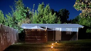 A backyard with a metal shed, a wooden fence, and a grassy area with ground lights.