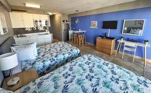 A compact studio apartment with two beds, a kitchenette, a dining area, and a living space with a TV and artwork. - New Wonderful Beach Front Studio in Daytona Beach! (Daytona Beach)