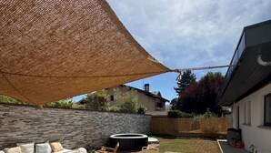 Eine Terrasse im Freien mit Tisch und Stühlen, einem großen gewebten Sonnenschutz und einer Steinwand.