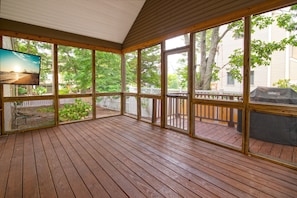 A covered outdoor deck with a view of a beach and a house.