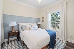 Une chambre à coucher avec un lit, des tables de chevet, une fenêtre avec des rideaux et une vue sur la verdure à l’extérieur.