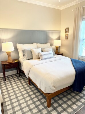 A neatly made bed with white bedding, flanked by two nightstands with lamps, in a room with a checkered floor and a window with curtains. - Meet Me In Oxford- 3BR -1 Mile from the Square (Oxford)