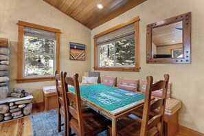 A cozy dining area with a wooden table, chairs, and a view of trees through the windows. - Mountain Khaya (Truckee)