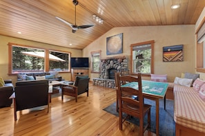 A spacious living room with a fireplace, wooden flooring, and large windows. - Mountain Khaya (Truckee)