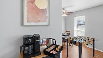 A kitchenette with a coffee maker, kettle, and coffee cups, a foosball table, and a framed abstract painting.
