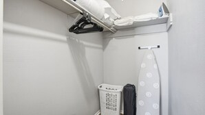 Een wasserette met een droogrek, een wasmand, een strijkplank en een douchegordijn.