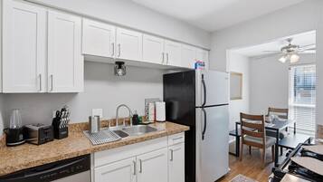A modern kitchen with white cabinets, a black refrigerator, a dishwasher, and a dining area with a table and chairs.