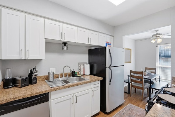 A modern kitchen with white cabinets, a black refrigerator, a dishwasher, and a dining area with a table and chairs.