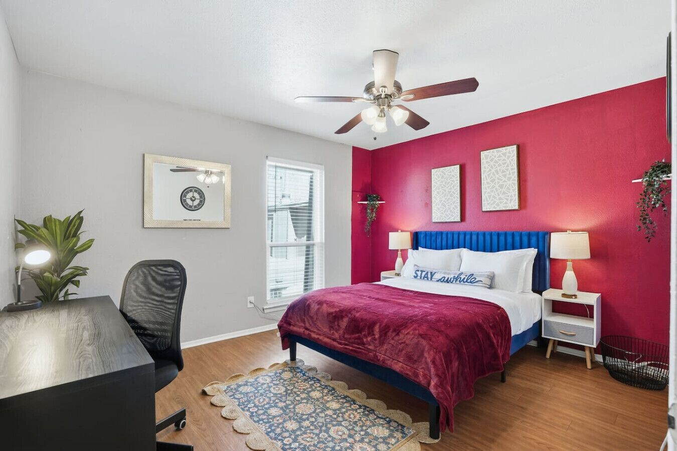 A bedroom with a bed, a desk, a chair, a ceiling fan, and a window.