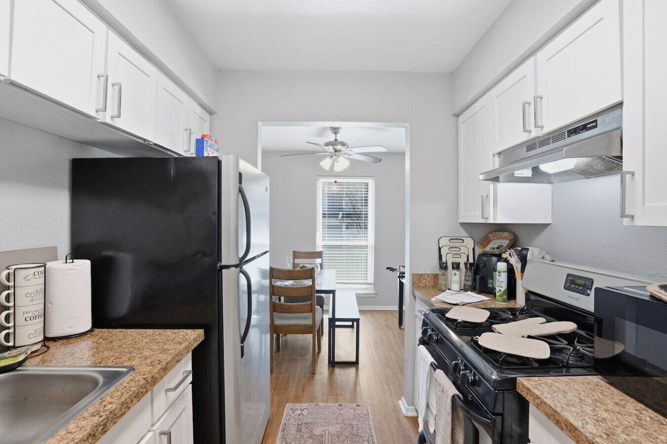 A compact kitchen with white cabinets, a black refrigerator, a stove, and a dining area with a table and chairs.