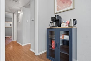 A hallway with a coffee maker, a kettle, and a cabinet containing coffee and tea products.