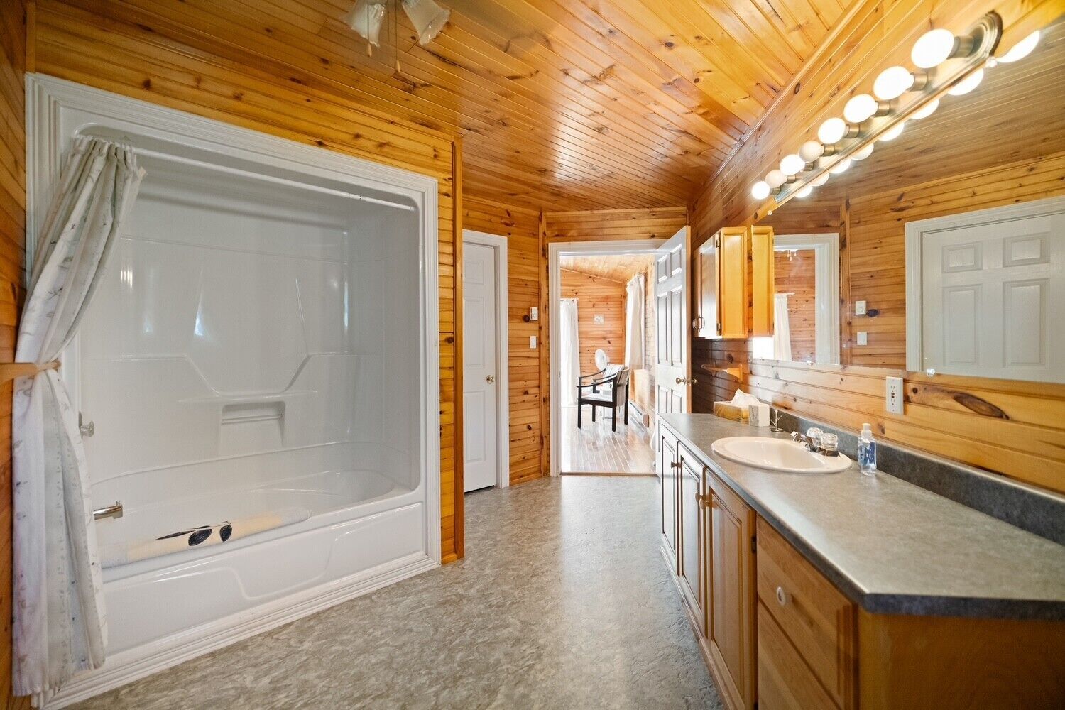 A wooden cabin interior with a large bathtub, a sink, and a mirror.