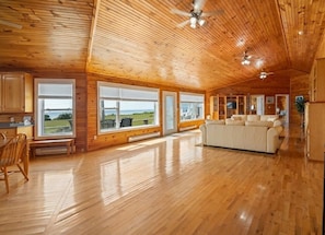 A spacious room with wooden floors and walls, large windows, a ceiling fan, and a white sofa.