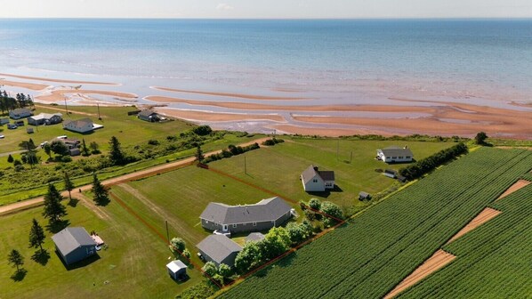 An aerial view of a coastal property with multiple buildings, green fields, and a beach.