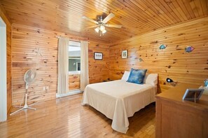 A wooden-paneled room with a bed, a ceiling fan, and a window with curtains.