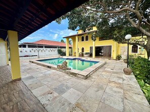 A swimming pool with a lion statue, a yellow building with a red roof, and a covered patio area. - Beach house with pool in Porto das Dunas, 8 suites, 5 min from the beach. (Aquiraz)