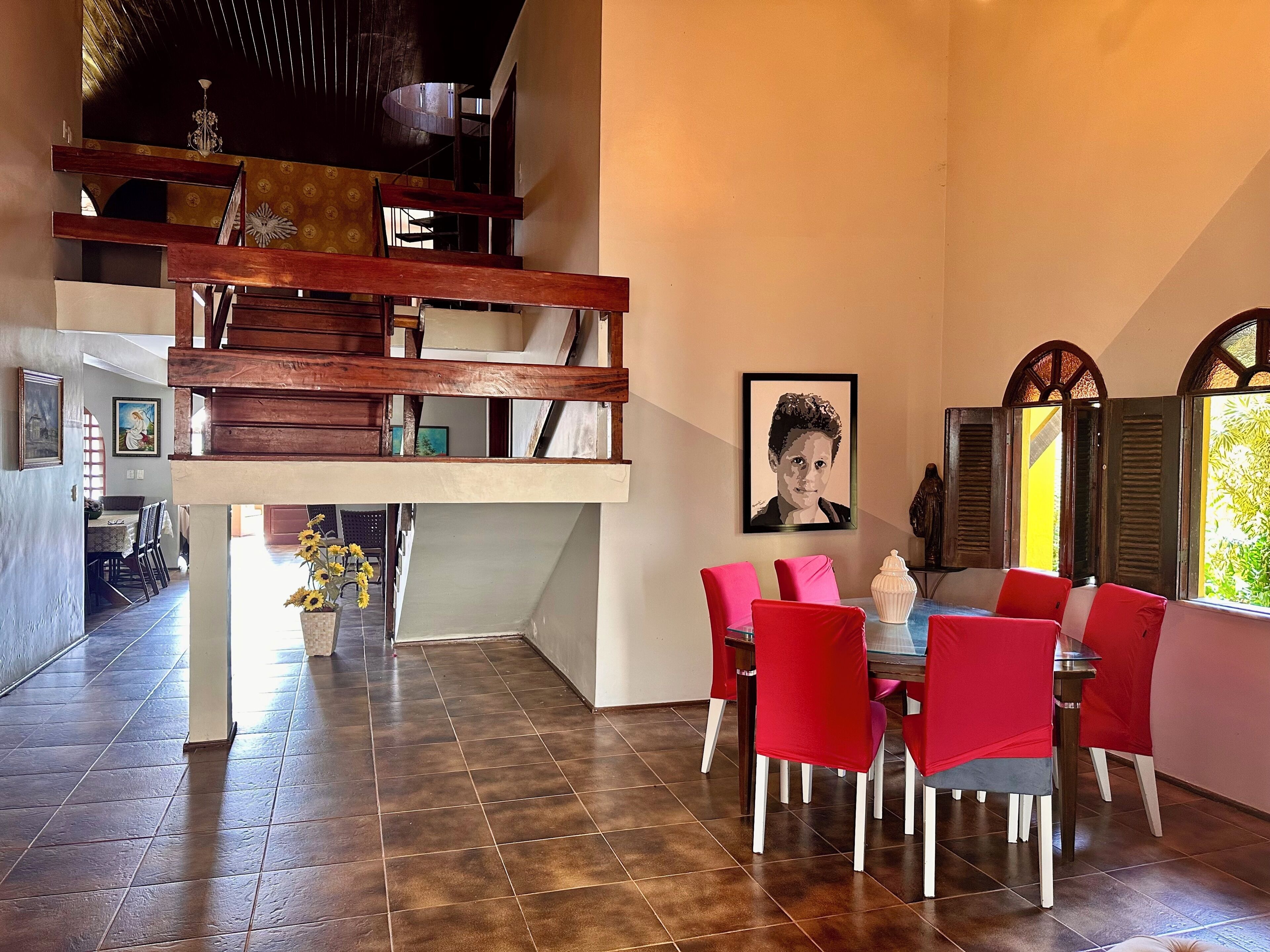 A dining area with a high ceiling, a staircase, and a dining table with red chairs.