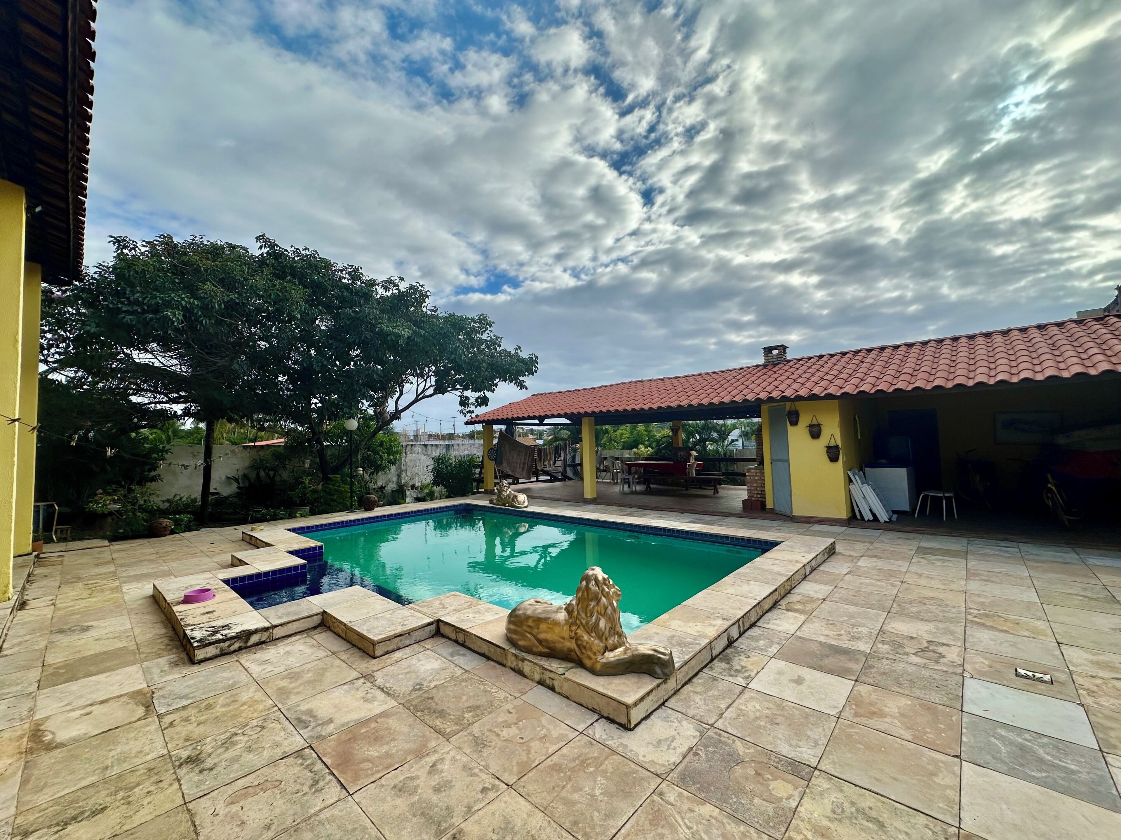 A swimming pool with a tiled deck, a stone sculpture, and a covered patio area.