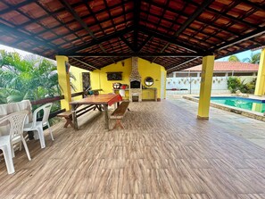 An outdoor patio with a brick fireplace, a pool, and a covered seating area. - Beach house with pool in Porto das Dunas, 8 suites, 5 min from the beach. (Aquiraz)