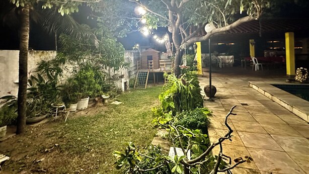 A well-lit outdoor area with a swimming pool, a grassy lawn, and various potted plants. - Beach house with pool in Porto das Dunas, 8 suites, 5 min from the beach. (Aquiraz)