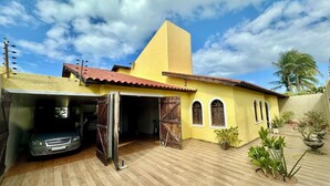 A yellow building with a red-tiled roof, a garage, and a paved courtyard with potted plants. - Beach house with pool in Porto das Dunas, 8 suites, 5 min from the beach. (Aquiraz)
