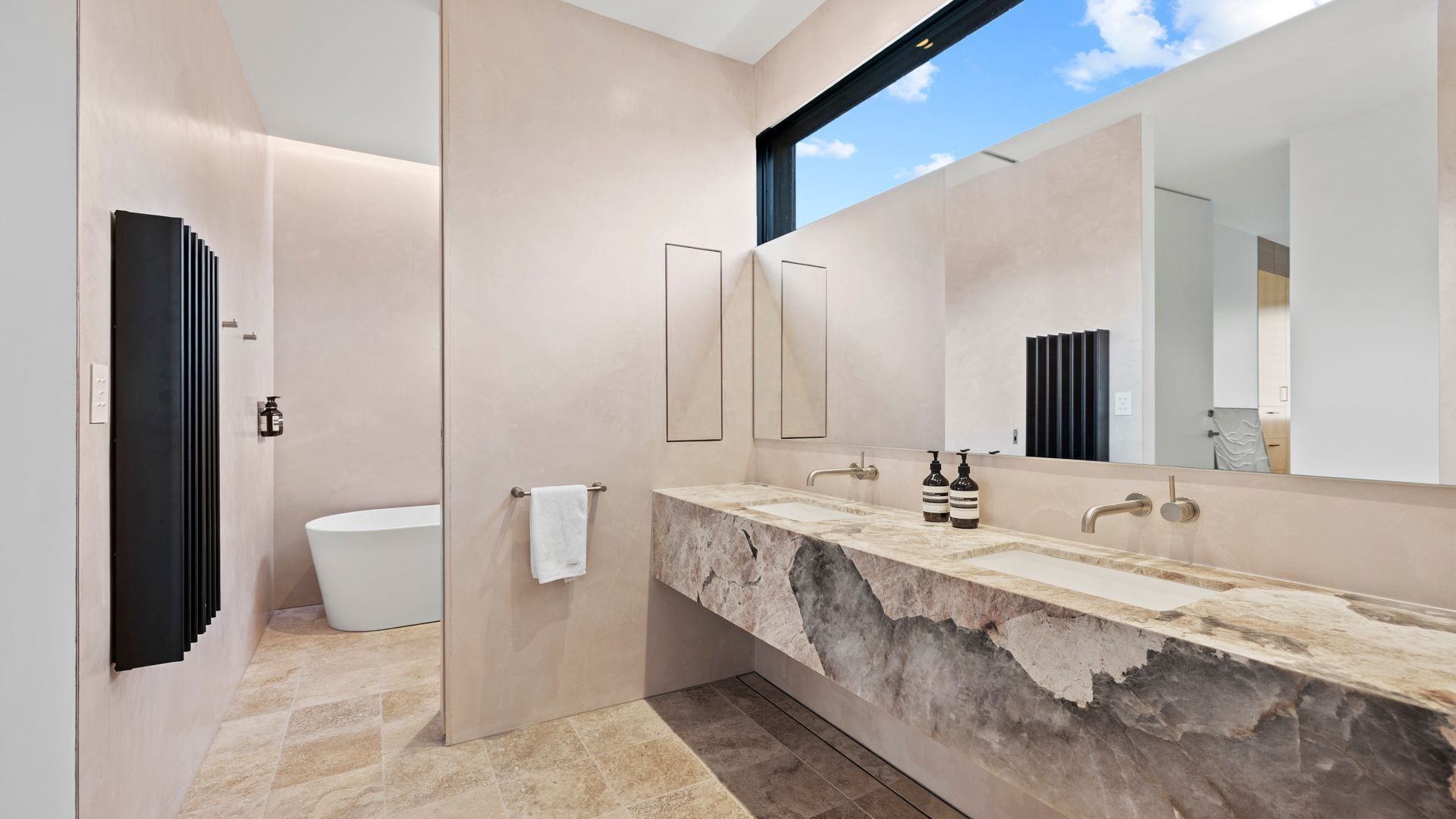 A modern bathroom with a marble vanity, a large mirror, and a toilet.