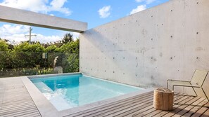 A modern outdoor swimming pool with a wooden deck, a metal chair, and a concrete wall. - Betula - Luxury Oasis in Wallaga Lake (Wallaga Lake)