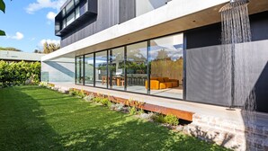 Ein modernes Haus mit einer verglasten Terrasse, Gartenmöbeln und einem Wasserspiel.