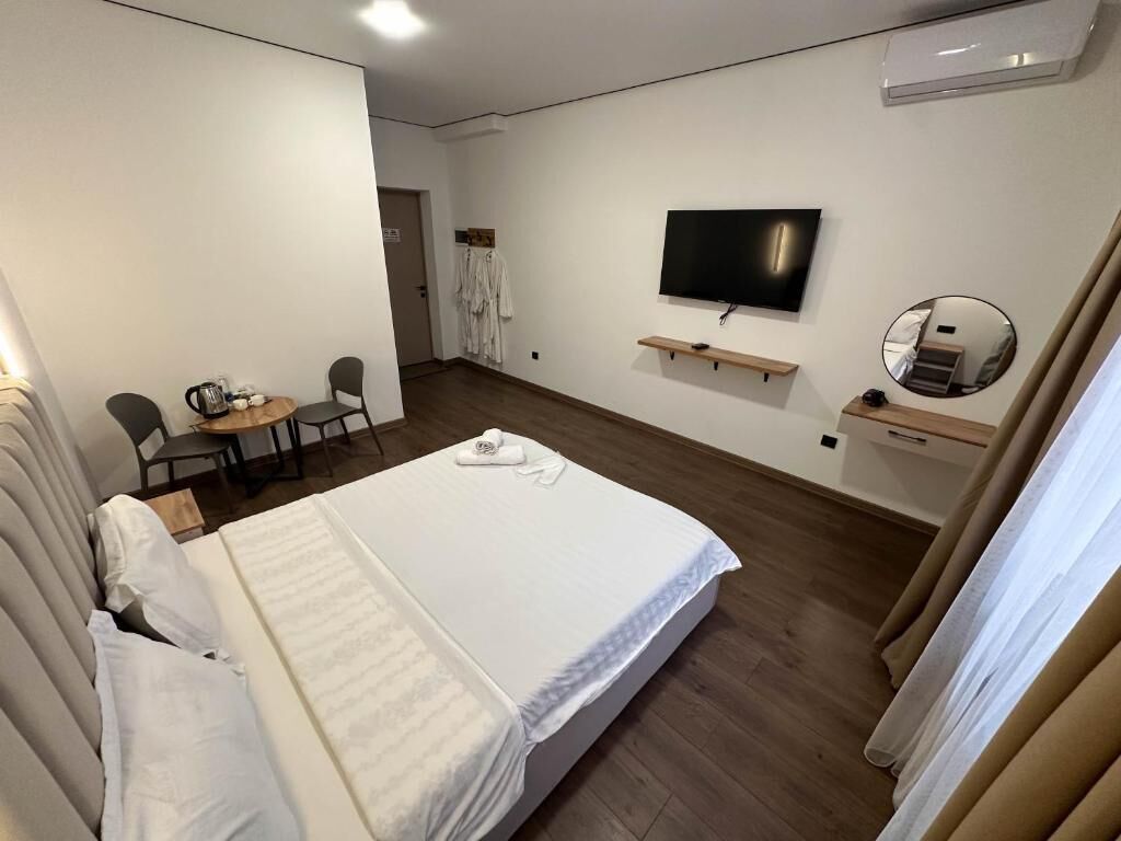 A hotel room with a bed, a TV, a small table with chairs, and a mirror.