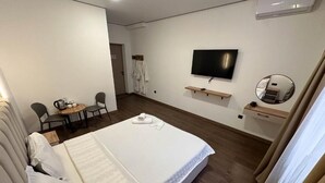 Ett hotellrum med en säng, en tv, ett litet bord med stolar och en spegel.