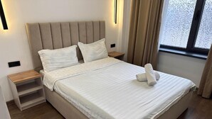 A neatly made bed with a headboard, a bedside table, and a window with curtains. - Gatsby Djal (Bishkek)