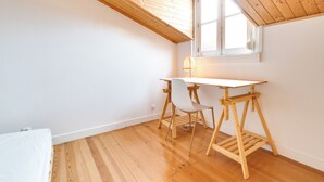 Una habitación con techo de madera inclinado, un escritorio blanco con una silla y una ventana.